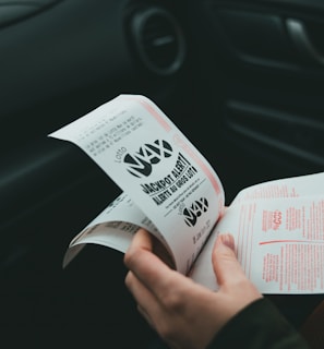 A person is holding and examining what appears to be lottery tickets inside a car. The image is focused on the tickets and the person's hands, with parts of the car interior visible in the background.