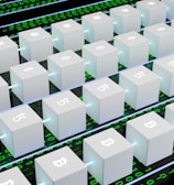 A digital artwork featuring multiple white cubic blocks aligned in a grid pattern, each displaying symbols of various cryptocurrencies like Bitcoin and Ethereum. The blocks are interconnected by glowing lines, set against a background of binary code in green and black.