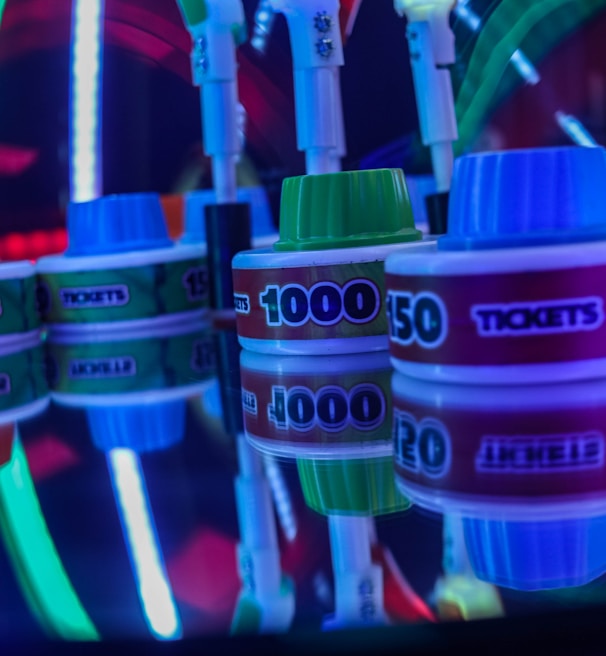 Stacks of tickets are arranged on a reflective surface, featuring various numerical values. Vibrant neon lights in red, blue, and green create a lively, arcade-like atmosphere, casting colorful reflections.